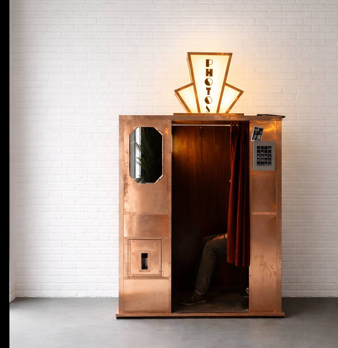 The Brasso booth, clad in copper with a cherry interior, a red curtain and an illuminated art deco PHOTOS sign